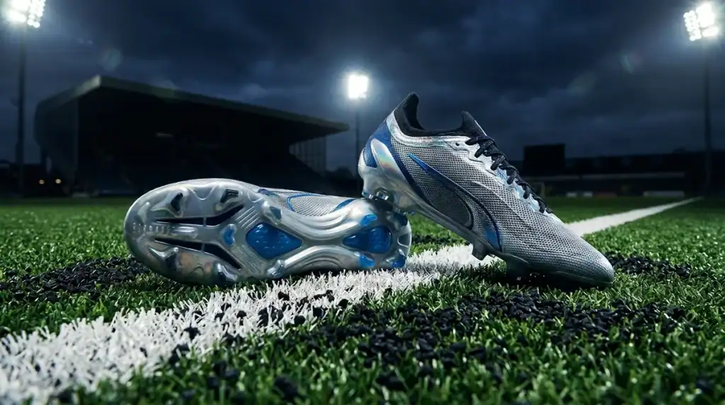 Gros plan au sol sur du gazon synthétique professionnel dans un stade de foot illuminé pour le comparatif chaussures 2026