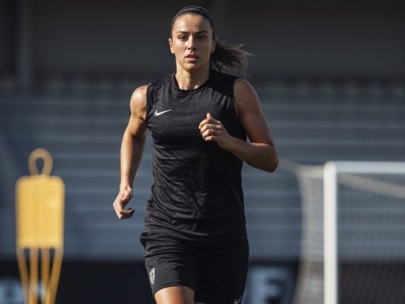 Footballeuse en plein effort portant un débardeur respirant noir sur un terrain d'entraînement
