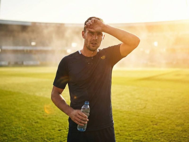 Gros plan sur un joueur de football en plein soleil, le visage en sueur, illustrant les conditions de jeu difficiles en été.