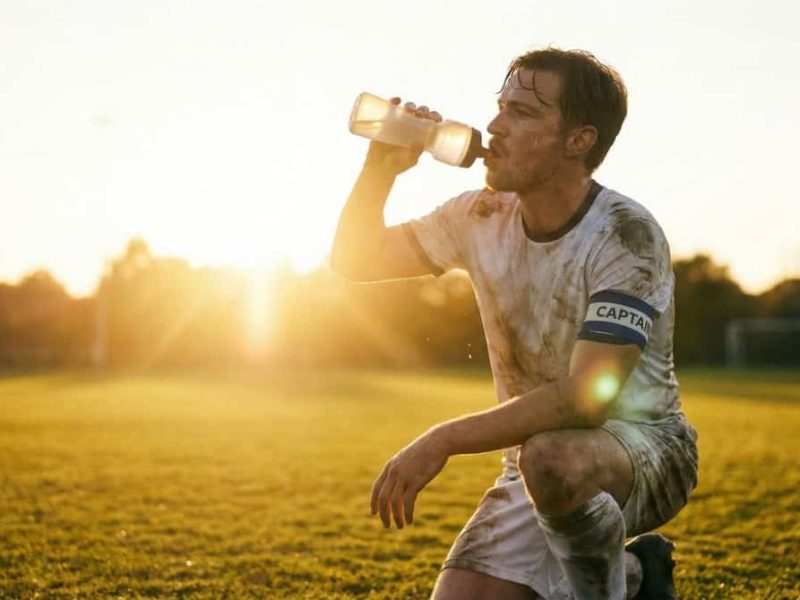 Footballeur s'hydratant avec une gourde lors d'une pause pendant un entraînement intensif.