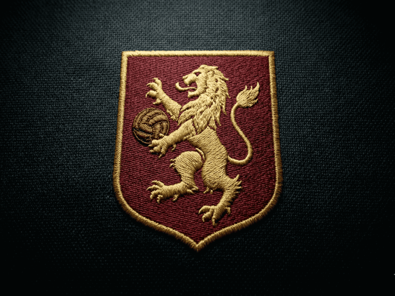 Gros plan artistique sur un blason de football brodé or et rouge sur un maillot texturé.