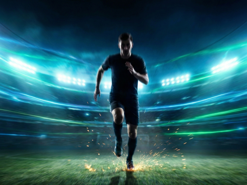 Joueur de football professionnel en plein sprint sous les projecteurs d'un stade, illustrant l'intensité et le besoin énergétique explosif du match.