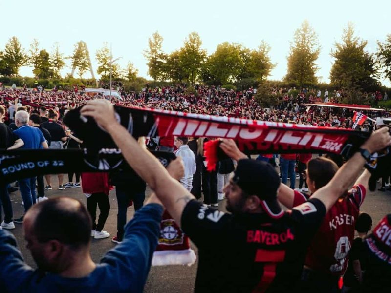 Une tribune de stade remplie de supporters passionnés chantant et tenant des écharpes en l'air.