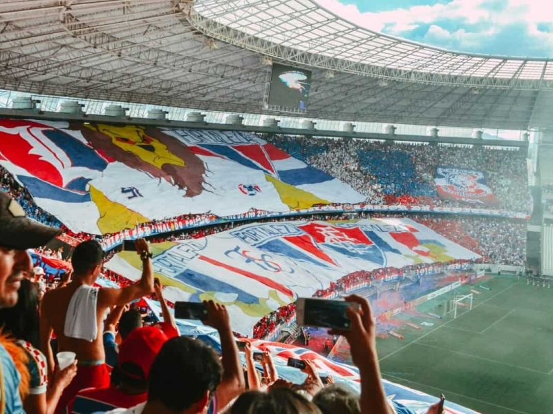 Immense tifo coloré déployé par des supporters dans un virage de stade de football, illustrant l'art de la banderole et la ferveur des tribunes.